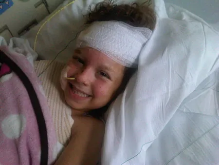 Caroline smiling from her hospital bed, her head bandaged